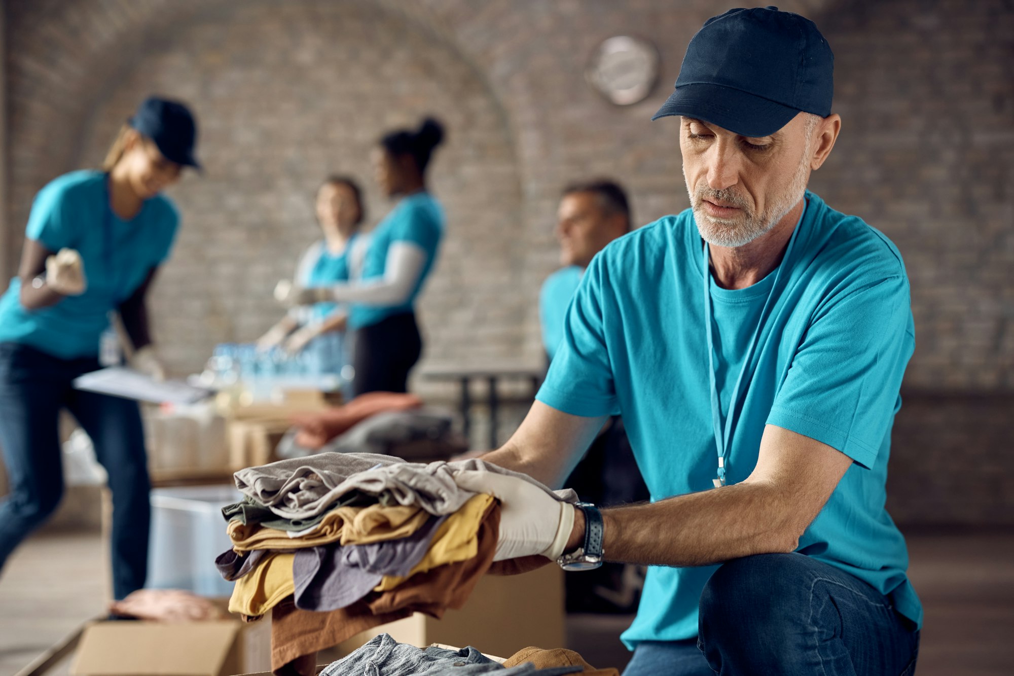 Mature man packing donated clothes in a box while volunteering at charity center.